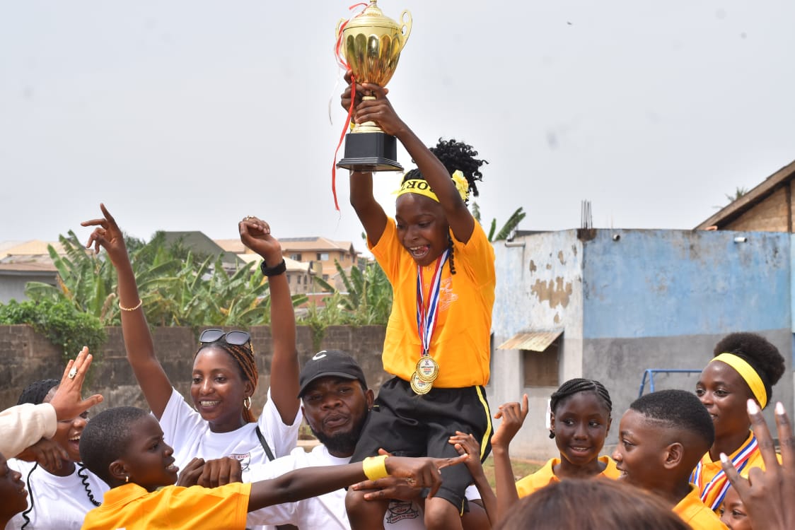 A pupil raising a trophy above her head, celebrated by schoolmates