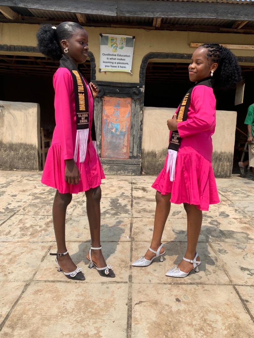 Two graduating pupils in pink gowns with class sashes